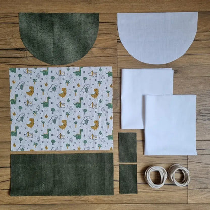 Kit prêt-à-coudre sac à dos pochon motif dinosaures avec base en velours côtelé vert, rabat arrondi, doublure blanche et cordons inclus. Kit couture complet avec tuto vidéo pour débutant.
