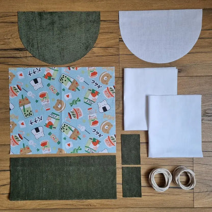Kit prêt-à-coudre pour sac à dos pochon avec rabat demi-lune, tissu à motifs kawaii japonais et base en velours côtelé vert, pièces prédécoupées et cordelettes incluses.