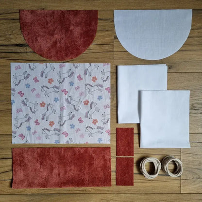 Kit prêt-à-coudre sac à dos pochon motif licornes sur fond blanc avec tissu velours côtelé terracotta, rabat arrondi assorti, doublure blanche et cordons écrus. Kit couture créatif et facile pour enfant ou débutant.