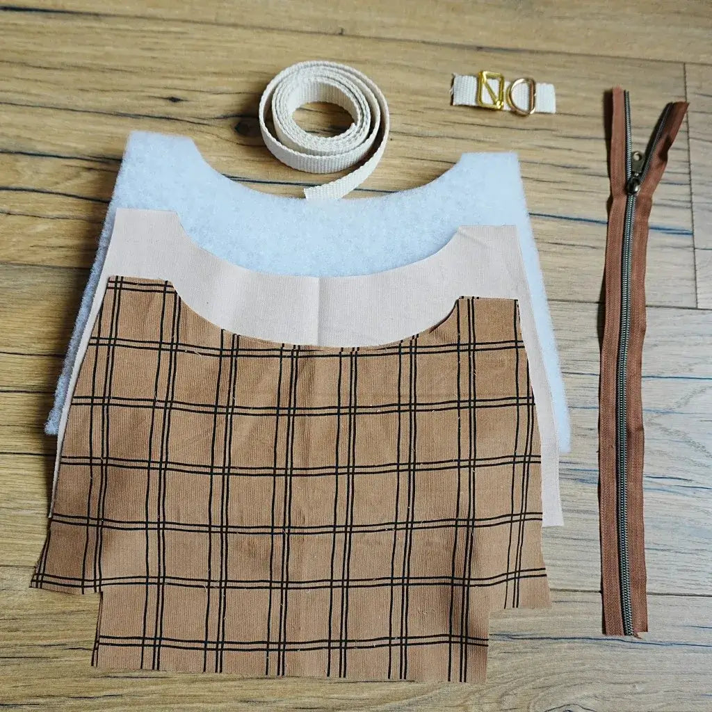 Kit prêt-à-coudre pour sac bandoulière à motif carreaux marron, comprenant pièces de tissu découpées, sangle en coton beige, fermeture éclair assortie et accessoires métalliques dorés. Idéal pour débutants et passionnés de couture, ce kit créatif permet de confectionner facilement un sac tendance et personnalisé, parfait pour un usage quotidien ou à offrir en cadeau fait main.