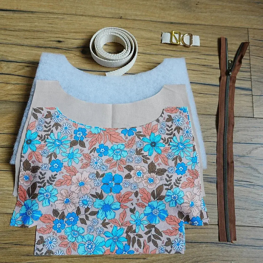Kit prêt-à-coudre pour réaliser un sac bandoulière motif hibiscus bleu et corail, comprenant les pièces de tissu fleuri pré-découpées, une sangle en coton beige, une fermeture éclair marron et des accessoires métalliques dorés. Ce kit créatif complet permet aux amateurs de couture de confectionner un sac tendance et personnalisé, idéal comme accessoire du quotidien ou cadeau fait main unique.