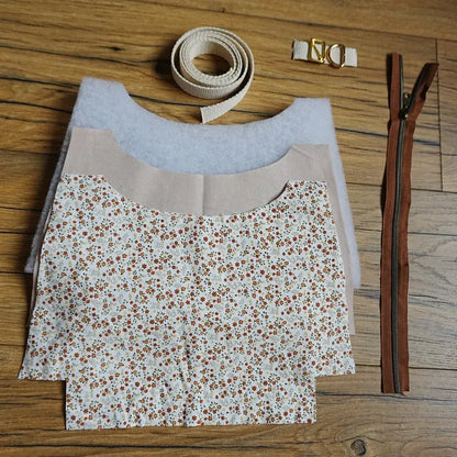 Kit de couture complet pour sac bandoulière motif fleuri prairie, avec tissu imprimé petites fleurs rouges et orangées, sangle en coton beige, fermeture éclair marron et accessoires métalliques dorés. Idéal pour les passionnés de DIY, ce kit prêt-à-coudre permet de créer un sac pratique et tendance, à la fois unique et personnalisé, parfait pour un usage quotidien ou comme cadeau fait main.