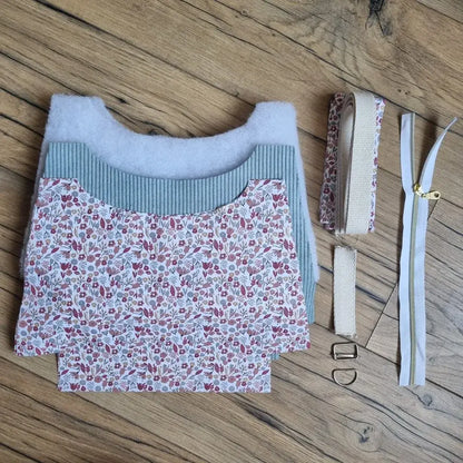 Kit prêt-à-coudre pour sac bandoulière en velours côtelé bleu clair, comprenant pièces de tissu extérieur, doublure à motif fleuri rouge et beige, sangle en coton, fermeture éclair blanche, boucles en métal et bande assortie. Disposé sur un fond en bois, ce kit complet est idéal pour réaliser un sac fait main au style doux, poétique et tendance. Convient aux couturières débutantes comme confirmées.