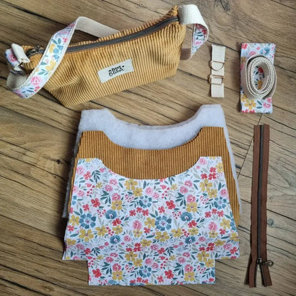 Kit prêt-à-coudre pour sac bandoulière en velours côtelé jaune, comprenant toutes les pièces nécessaires : tissu extérieur et doublure fleurie découpés, sangle, boucle, fermeture éclair et bande décorative. Le sac fini est présenté en haut de l’image comme exemple. Parfait pour les couturières de niveau intermédiaire souhaitant créer un sac fait main tendance et personnalisé.
