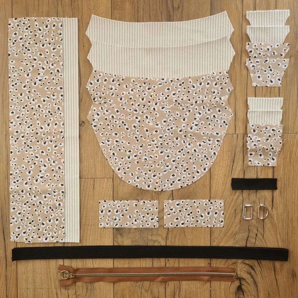 Kit "prêt à coudre" pour un sac demi-lune en velours côtelé au coloris beige avec une doublure en tissu à motif léopard. L'ensemble des pièces de tissu, déjà prédécoupées aux bonnes dimensions, sont disposées au sol et comprennent neuf pièces en tissu à motif léopard et sept pièces en velours côtelé de couleur beige ainsi qu'une fermeture éclair marron et une sangle noire.