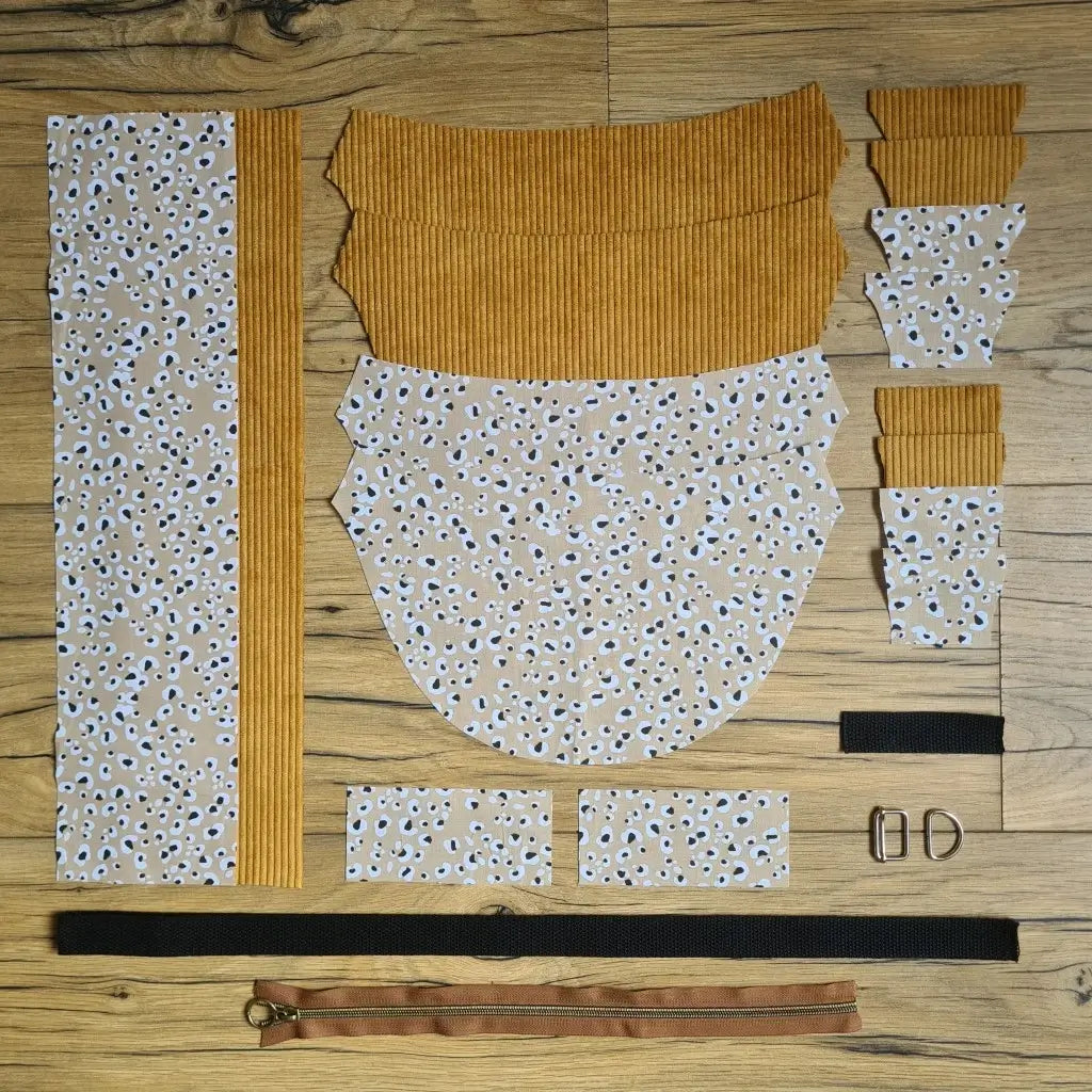 Kit "prêt à coudre" pour un sac demi-lune en velours côtelé au coloris jaune avec une doublure en tissu à motif léopard. L'ensemble des pièces de tissu, déjà prédécoupées aux bonnes dimensions, sont disposées au sol et comprennent neuf pièces en tissu à motif léopard et sept pièces en velours côtelé de couleur jaune ainsi qu'une fermeture éclair marron et une sangle noire.