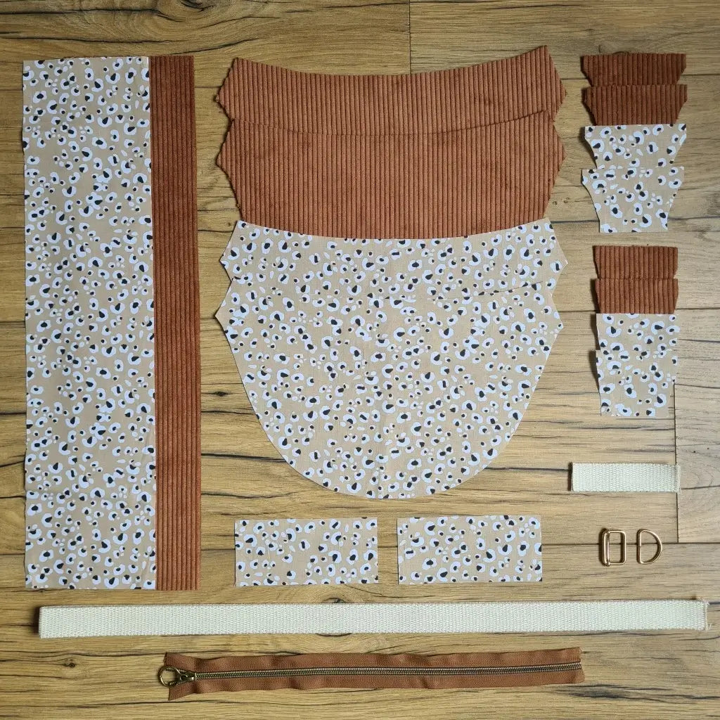 Kit "prêt à coudre" pour un sac demi-lune en velours côtelé au coloris marron avec une doublure en tissu à motif léopard. L'ensemble des pièces de tissu, déjà prédécoupées aux bonnes dimensions, sont disposées au sol et comprennent neuf pièces en tissu à motif léopard et sept pièces en velours côtelé de couleur marron ainsi qu'une fermeture éclair marron et une sangle beige.