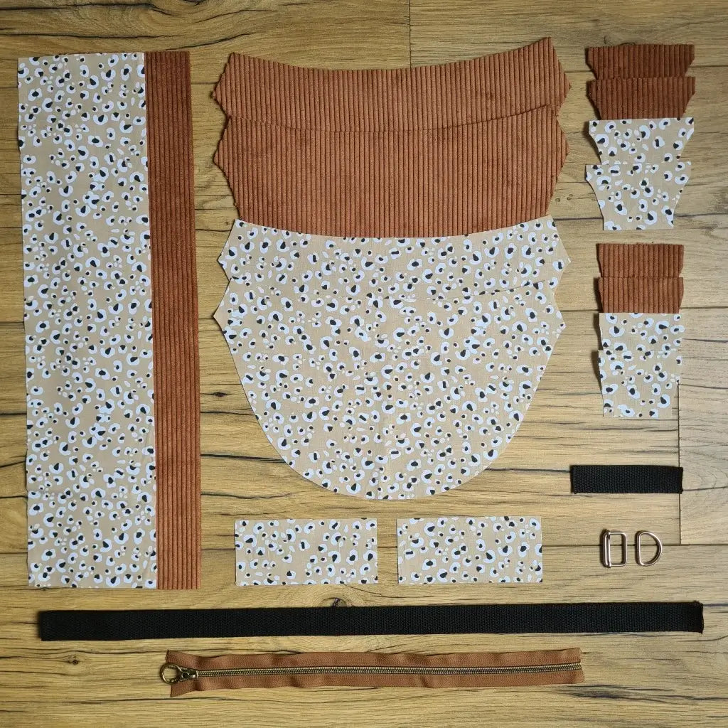 Kit "prêt à coudre" pour un sac demi-lune en velours côtelé au coloris marron avec une doublure en tissu à motif léopard. L'ensemble des pièces de tissu, déjà prédécoupées aux bonnes dimensions, sont disposées au sol et comprennent neuf pièces en tissu à motif léopard et sept pièces en velours côtelé de couleur marron ainsi qu'une fermeture éclair marron et une sangle noire.