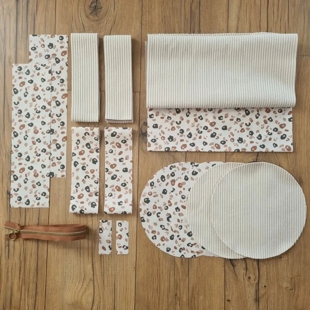 Kit "prêt à coudre" pour un sac polochon en velours côtelé au coloris beige avec une doublure en tissu à motif léopard. L'ensemble des pièces de tissu, déjà prédécoupées aux bonnes dimensions, sont disposées au sol et comprennent neuf pièces en tissu à motif léopard et cinq pièces en velours côtelé de couleur beige ainsi qu'une fermeture éclair marron.