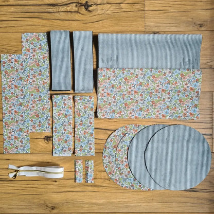 Kit "prêt à coudre" pour un sac polochon en velours côtelé au coloris bleu ciel avec une doublure en tissu à motif fleuri. L'ensemble des pièces de tissu, déjà prédécoupées aux bonnes dimensions, sont disposées au sol et comprennent neuf pièces en tissu à motif fleuri et cinq pièces en velours côtelé de couleur bleu ciel ainsi qu'une fermeture éclair blanche.
