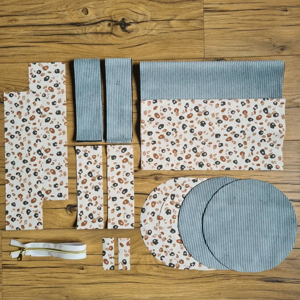 Kit "prêt à coudre" pour un sac polochon en velours côtelé au coloris bleu ciel avec une doublure en tissu à motif léopard. L'ensemble des pièces de tissu, déjà prédécoupées aux bonnes dimensions, sont disposées au sol et comprennent neuf pièces en tissu à motif léopard et cinq pièces en velours côtelé de couleur bleu ciel ainsi qu'une fermeture éclair blanche.