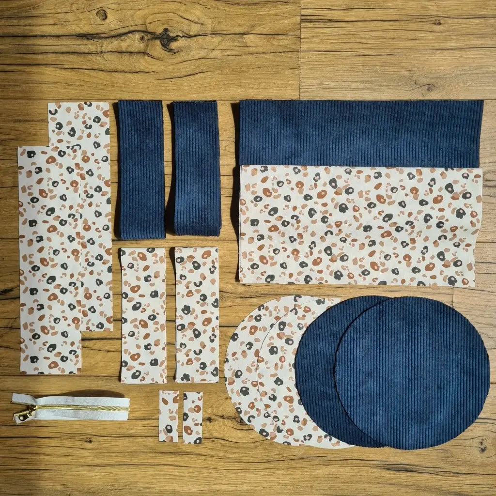 Kit "prêt à coudre" pour un sac polochon en velours côtelé au coloris bleu foncé avec une doublure en tissu à motif léopard. L'ensemble des pièces de tissu, déjà prédécoupées aux bonnes dimensions, sont disposées au sol et comprennent neuf pièces en tissu à motif léopard et cinq pièces en velours côtelé de couleur bleu foncé ainsi qu'une fermeture éclair blanche.