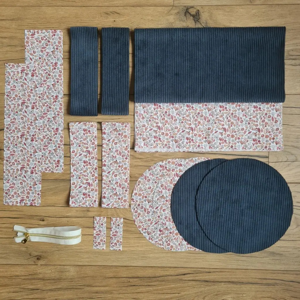 Kit "prêt à coudre" pour un sac polochon en velours côtelé au coloris bleu foncé avec une doublure en tissu à motif liberty. L'ensemble des pièces de tissu, déjà prédécoupées aux bonnes dimensions, sont disposées au sol et comprennent neuf pièces en tissu à motif liberty et cinq pièces en velours côtelé de couleur bleu foncé ainsi qu'une fermeture éclair blanche.