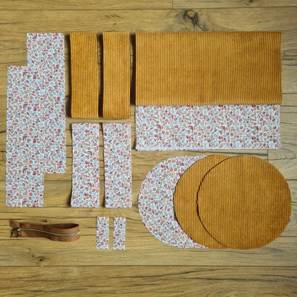 Kit "prêt à coudre" pour un sac polochon en velours côtelé au coloris jaune avec une doublure en tissu à motif liberty. L'ensemble des pièces de tissu, déjà prédécoupées aux bonnes dimensions, sont disposées au sol et comprennent neuf pièces en tissu à motif liberty et cinq pièces en velours côtelé de couleur jaune ainsi qu'une fermeture éclair marron.