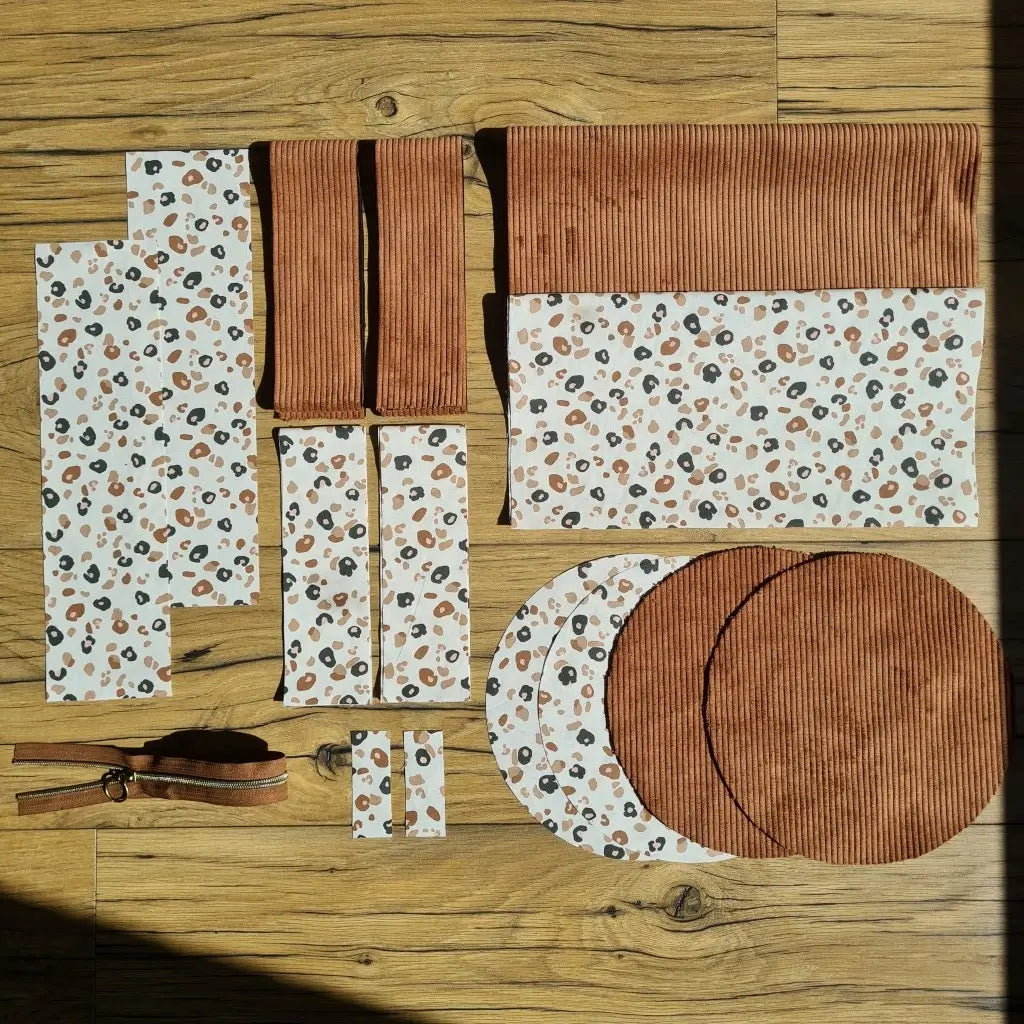 Kit "prêt à coudre" pour un sac polochon en velours côtelé au coloris marron avec une doublure en tissu à motif léopard. L'ensemble des pièces de tissu, déjà prédécoupées aux bonnes dimensions, sont disposées au sol et comprennent neuf pièces en tissu à motif léopard et cinq pièces en velours côtelé de couleur marron ainsi qu'une fermeture éclair marron.