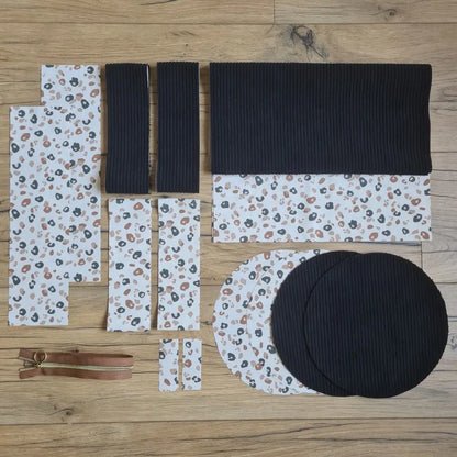 Kit "prêt à coudre" pour un sac polochon en velours côtelé au coloris noir avec une doublure en tissu à motif léopard. L'ensemble des pièces de tissu, déjà prédécoupées aux bonnes dimensions, sont disposées au sol et comprennent neuf pièces en tissu à motif léopard et cinq pièces en velours côtelé de couleur noir ainsi qu'une fermeture éclair marron.