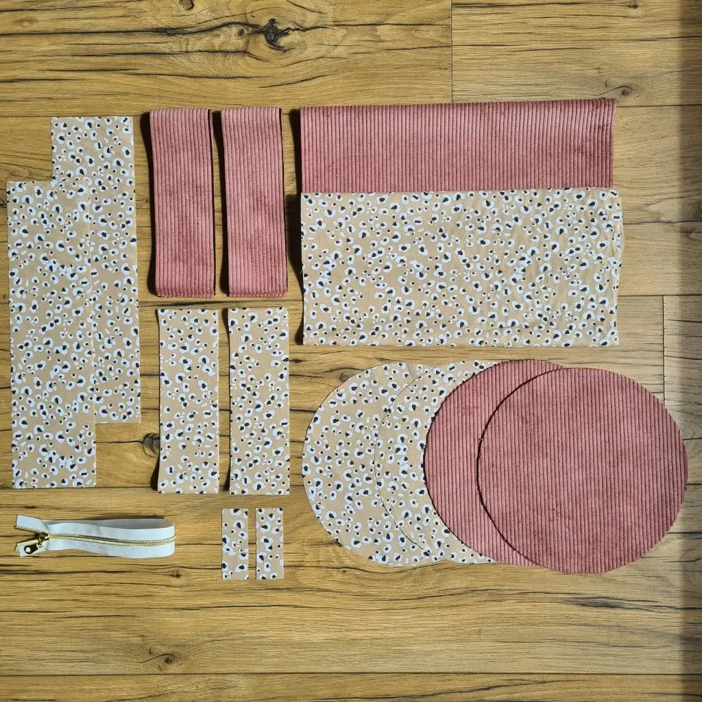 Kit "prêt à coudre" pour un sac polochon en velours côtelé au coloris rose avec une doublure en tissu à motif léopard. L'ensemble des pièces de tissu, déjà prédécoupées aux bonnes dimensions, sont disposées au sol et comprennent neuf pièces en tissu à motif léopard et cinq pièces en velours côtelé de couleur rose ainsi qu'une fermeture éclair blanche.