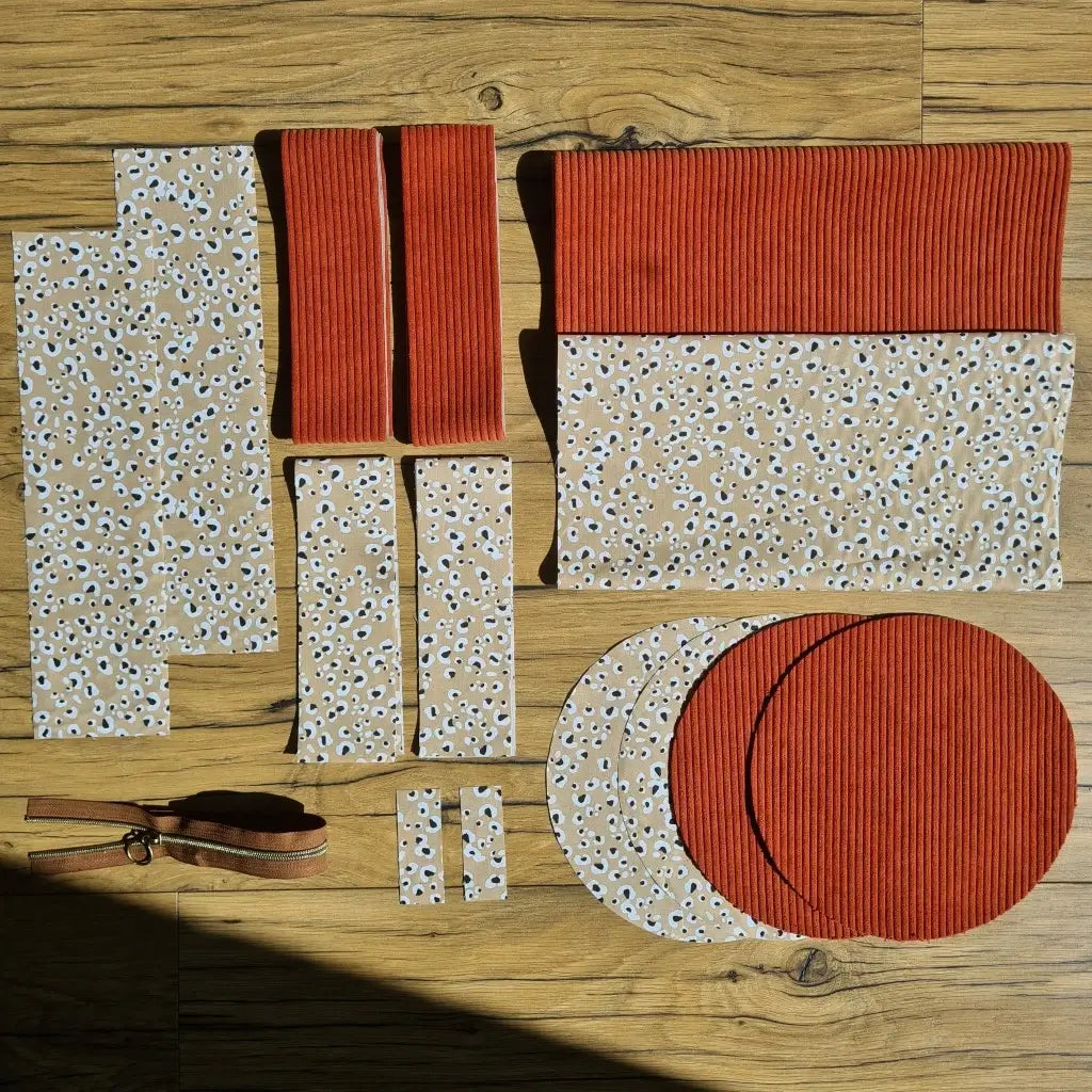 Kit "prêt à coudre" pour un sac polochon en velours côtelé au coloris terracotta avec une doublure en tissu à motif léopard. L'ensemble des pièces de tissu, déjà prédécoupées aux bonnes dimensions, sont disposées au sol et comprennent neuf pièces en tissu à motif léopard et cinq pièces en velours côtelé de couleur terracotta ainsi qu'une fermeture éclair marron.