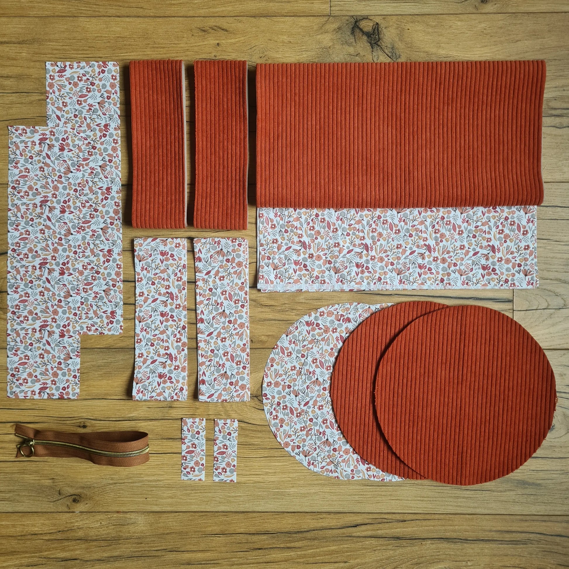 Kit "prêt à coudre" pour un sac polochon en velours côtelé au coloris terracotta avec une doublure en tissu à motif liberty. L'ensemble des pièces de tissu, déjà prédécoupées aux bonnes dimensions, sont disposées au sol et comprennent neuf pièces en tissu à motif liberty et cinq pièces en velours côtelé de couleur terracotta ainsi qu'une fermeture éclair marron.