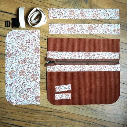 Kit prêt à coudre pour tablier ceinture comprenant des pièces en velours côtelé marron et coton imprimé oriental, une fermeture éclair marron, une sangle en coton écru avec boucle de réglage et clip plastique, disposés à plat sur un sol en bois. Ensemble complet idéal pour créer un tablier pratique et élégant, parfait pour la couture créative et les loisirs faits main.