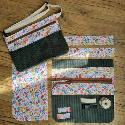 Kit prêt-à-coudre pour réaliser un tablier ceinture personnalisable, composé de pièces de tissu en velours côtelé vert et coton fleuri multicolore, d'une fermeture éclair, d'une sangle en coton écru et de boucles en plastique. Ce kit DIY permet de confectionner une ceinture de couture pratique avec poches et compartiments, idéale pour les créatrices, couturières ou les maîtresses. La photo montre le rendu final aux côtés des éléments à coudre.