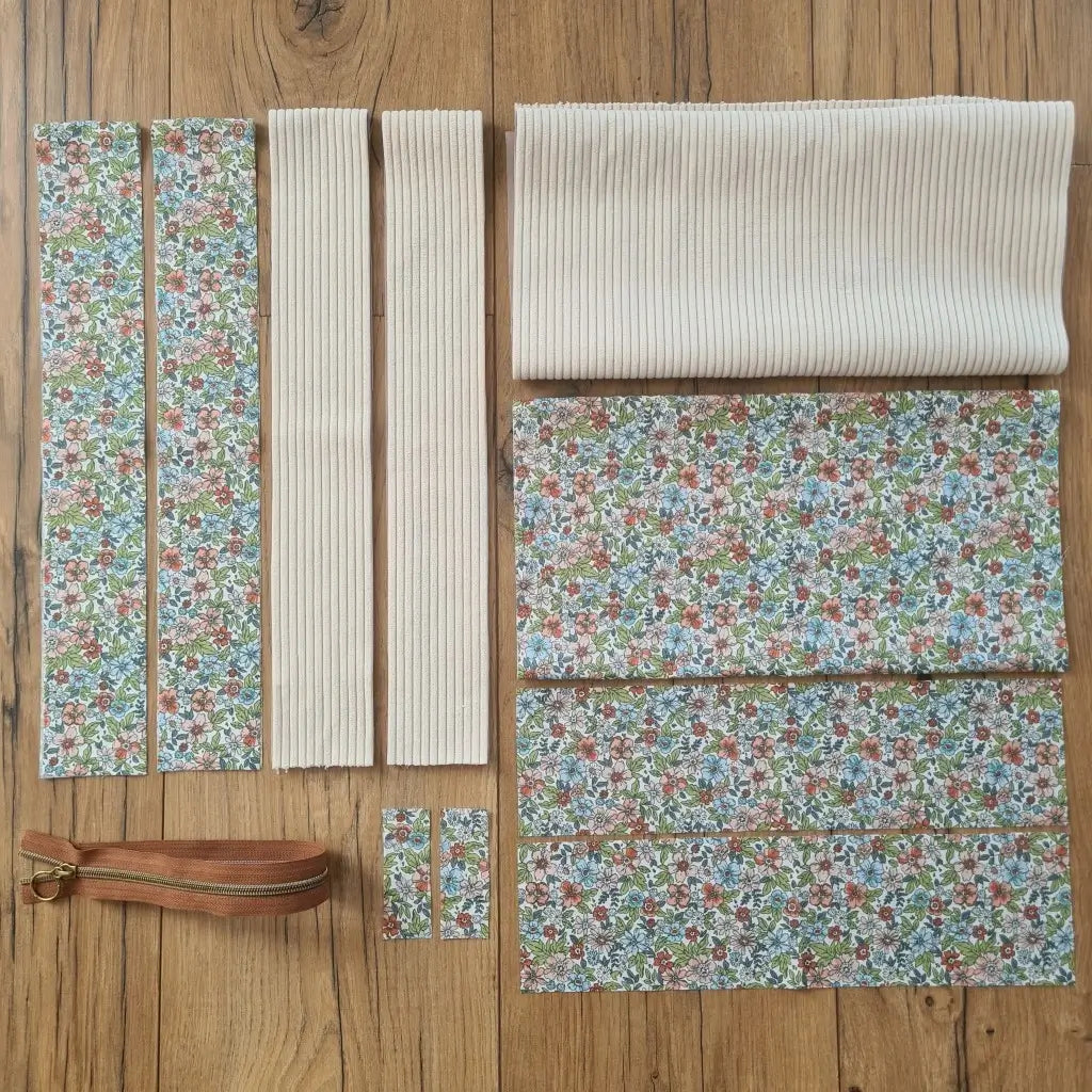 Kit "prêt à coudre" pour un tote-bag en velours côtelé au coloris beige avec une doublure en tissu à motif fleuri. L'ensemble des pièces de tissu, déjà prédécoupées aux bonnes dimensions, sont disposées au sol et comprennent sept pièces en tissu à motif fleuri et trois pièces en velours côtelé de couleur beige ainsi qu'une fermeture éclair marron.