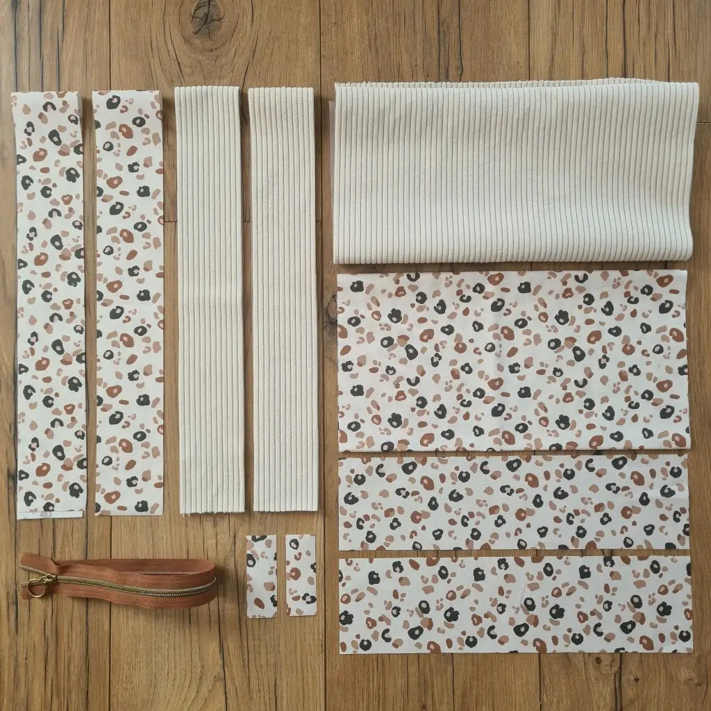 Kit "prêt à coudre" pour un tote-bag en velours côtelé au coloris beige avec une doublure en tissu à motif léopard. L'ensemble des pièces de tissu, déjà prédécoupées aux bonnes dimensions, sont disposées au sol et comprennent sept pièces en tissu à motif léopard et trois pièces en velours côtelé de couleur beige ainsi qu'une fermeture éclair marron.