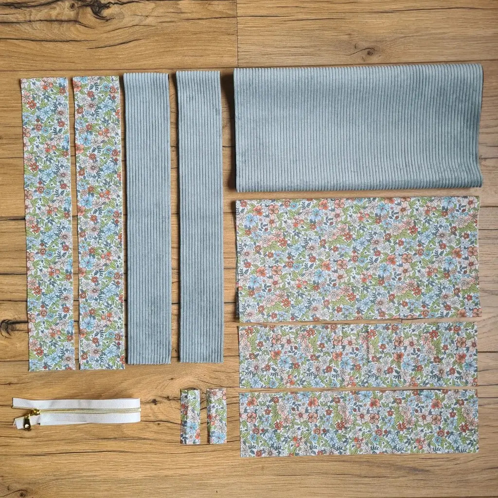 Kit "prêt à coudre" pour un tote-bag en velours côtelé au coloris bleu ciel avec une doublure en tissu à motif fleuri. L'ensemble des pièces de tissu, déjà prédécoupées aux bonnes dimensions, sont disposées au sol et comprennent sept pièces en tissu à motif fleuri et trois pièces en velours côtelé de couleur bleu ciel ainsi qu'une fermeture éclair blanche.