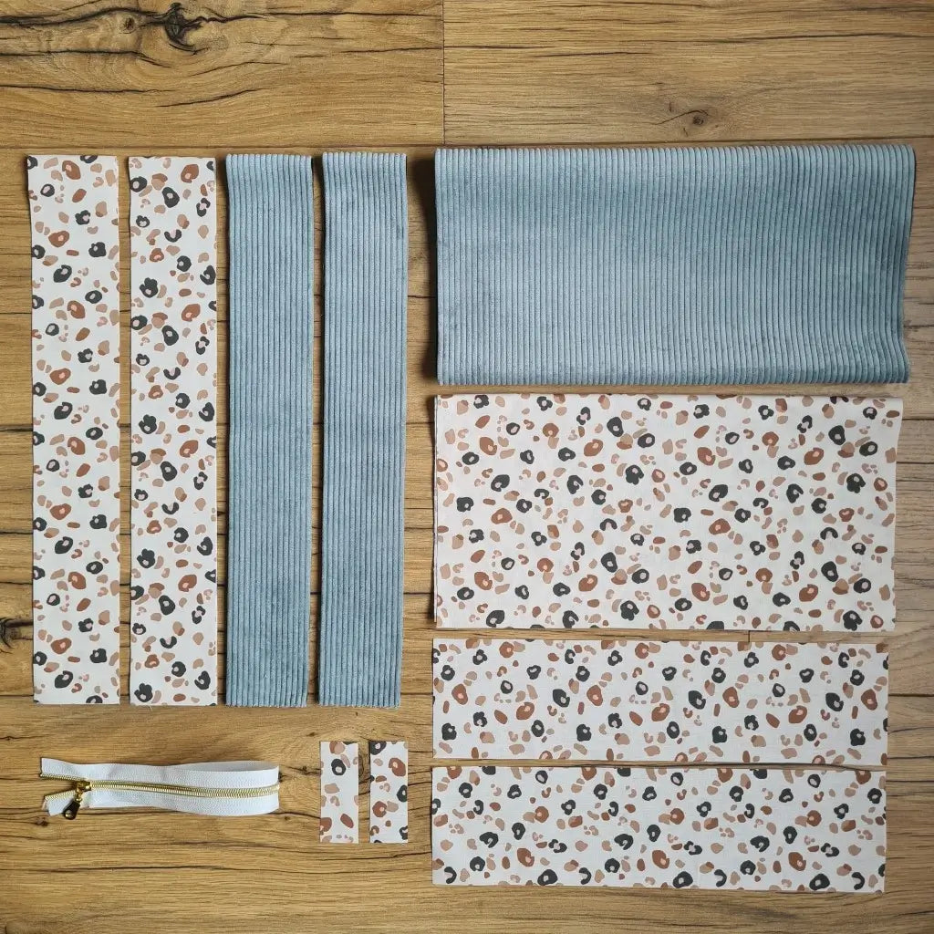 Kit "prêt à coudre" pour un tote-bag en velours côtelé au coloris bleu ciel avec une doublure en tissu à motif léopard. L'ensemble des pièces de tissu, déjà prédécoupées aux bonnes dimensions, sont disposées au sol et comprennent sept pièces en tissu à motif léopard et trois pièces en velours côtelé de couleur bleu ciel ainsi qu'une fermeture éclair blanche.