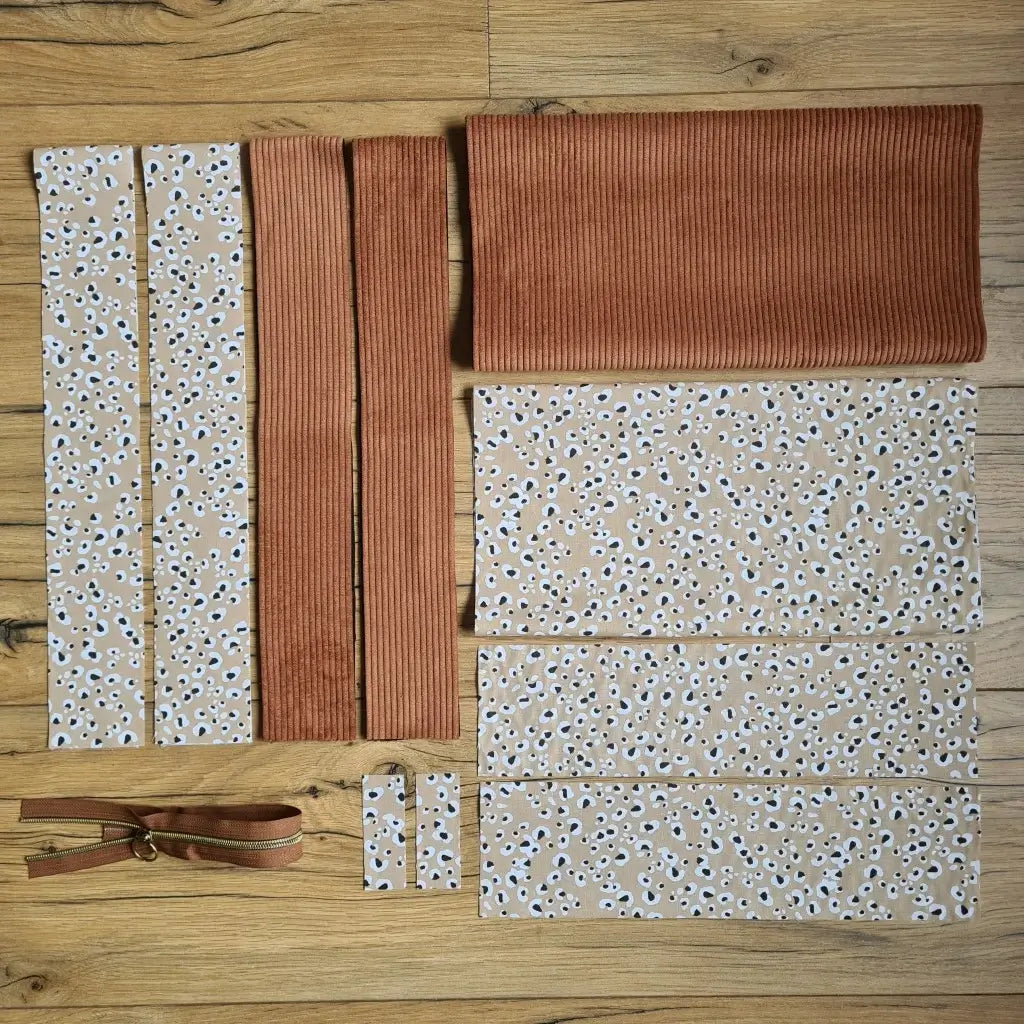 Kit "prêt à coudre" pour un tote-bag en velours côtelé au coloris marron avec une doublure en tissu à motif léopard. L'ensemble des pièces de tissu, déjà prédécoupées aux bonnes dimensions, sont disposées au sol et comprennent sept pièces en tissu à motif léopard et trois pièces en velours côtelé de couleur marron ainsi qu'une fermeture éclair marron.