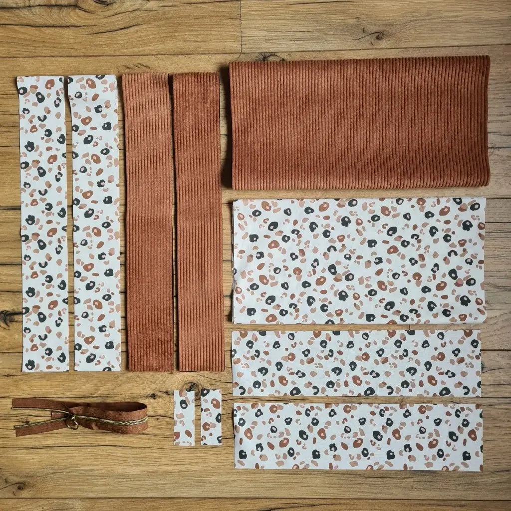 Kit "prêt à coudre" pour un tote-bag en velours côtelé au coloris marron avec une doublure en tissu à motif léopard. L'ensemble des pièces de tissu, déjà prédécoupées aux bonnes dimensions, sont disposées au sol et comprennent sept pièces en tissu à motif léopard et trois pièces en velours côtelé de couleur marron ainsi qu'une fermeture éclair marron.