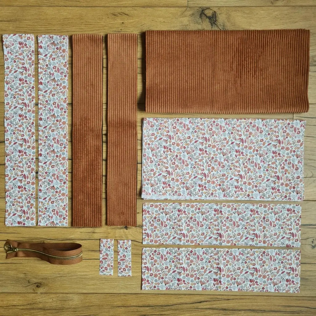 Kit "prêt à coudre" pour un tote-bag en velours côtelé au coloris marron avec une doublure en tissu à motif liberty. L'ensemble des pièces de tissu, déjà prédécoupées aux bonnes dimensions, sont disposées au sol et comprennent sept pièces en tissu à motif liberty et trois pièces en velours côtelé de couleur marron ainsi qu'une fermeture éclair marron.