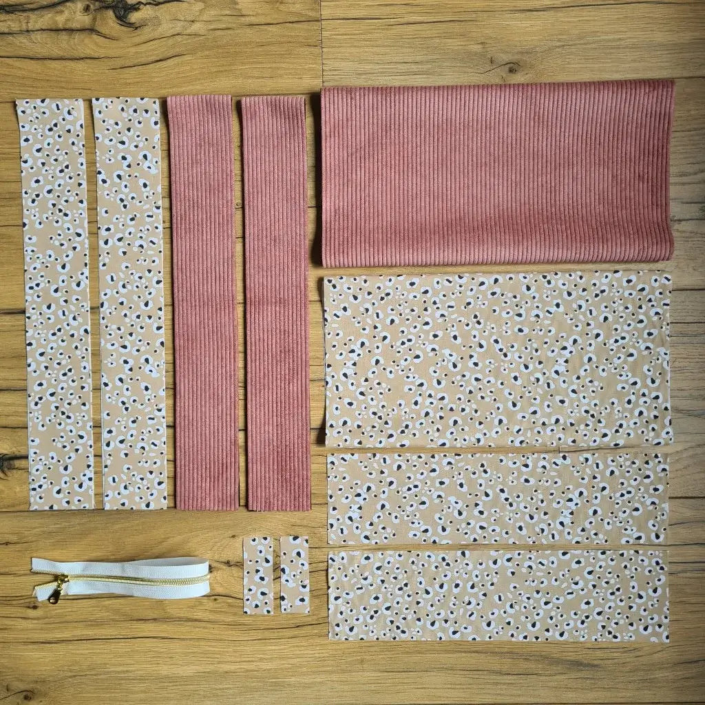 Kit "prêt à coudre" pour un tote-bag en velours côtelé au coloris rose avec une doublure en tissu à motif léopard. L'ensemble des pièces de tissu, déjà prédécoupées aux bonnes dimensions, sont disposées au sol et comprennent sept pièces en tissu à motif léopard et trois pièces en velours côtelé de couleur rose ainsi qu'une fermeture éclair blanche.