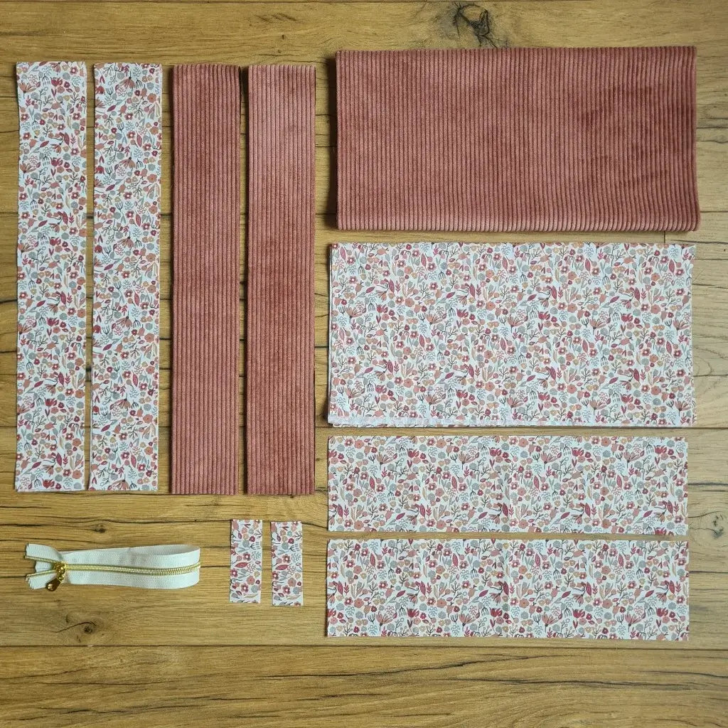 Kit "prêt à coudre" pour un tote-bag en velours côtelé au coloris rose avec une doublure en tissu à motif liberty. L'ensemble des pièces de tissu, déjà prédécoupées aux bonnes dimensions, sont disposées au sol et comprennent sept pièces en tissu à motif liberty et trois pièces en velours côtelé de couleur rose ainsi qu'une fermeture éclair beige.