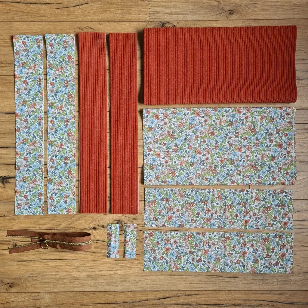 Kit "prêt à coudre" pour un tote-bag en velours côtelé au coloris terracotta avec une doublure en tissu à motif fleuri. L'ensemble des pièces de tissu, déjà prédécoupées aux bonnes dimensions, sont disposées au sol et comprennent sept pièces en tissu à motif fleuri et trois pièces en velours côtelé de couleur terracotta ainsi qu'une fermeture éclair marron.