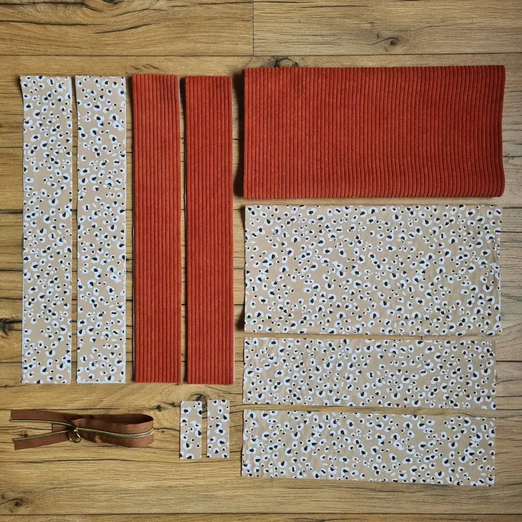 Kit "prêt à coudre" pour un tote-bag en velours côtelé au coloris terracotta avec une doublure en tissu à motif léopard. L'ensemble des pièces de tissu, déjà prédécoupées aux bonnes dimensions, sont disposées au sol et comprennent sept pièces en tissu à motif léopard et trois pièces en velours côtelé de couleur terracotta ainsi qu'une fermeture éclair marron.