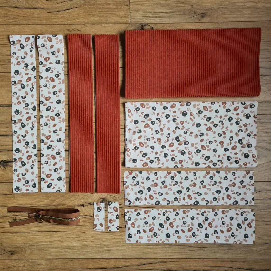 Kit "prêt à coudre" pour un tote-bag en velours côtelé au coloris terracotta avec une doublure en tissu à motif léopard. L'ensemble des pièces de tissu, déjà prédécoupées aux bonnes dimensions, sont disposées au sol et comprennent sept pièces en tissu à motif léopard et trois pièces en velours côtelé de couleur terracotta ainsi qu'une fermeture éclair marron.