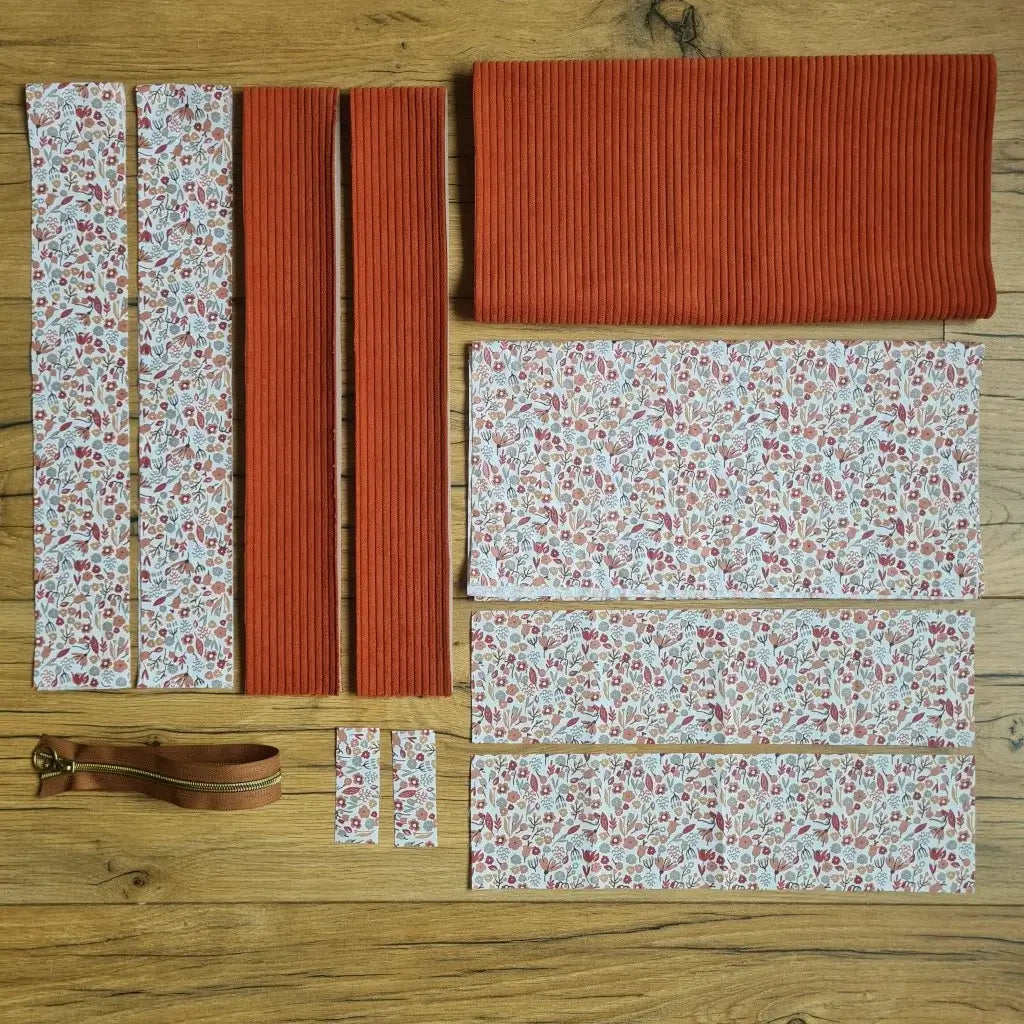 Kit "prêt à coudre" pour un tote-bag en velours côtelé au coloris terracotta avec une doublure en tissu à motif liberty. L'ensemble des pièces de tissu, déjà prédécoupées aux bonnes dimensions, sont disposées au sol et comprennent sept pièces en tissu à motif liberty et trois pièces en velours côtelé de couleur terracotta ainsi qu'une fermeture éclair marron.