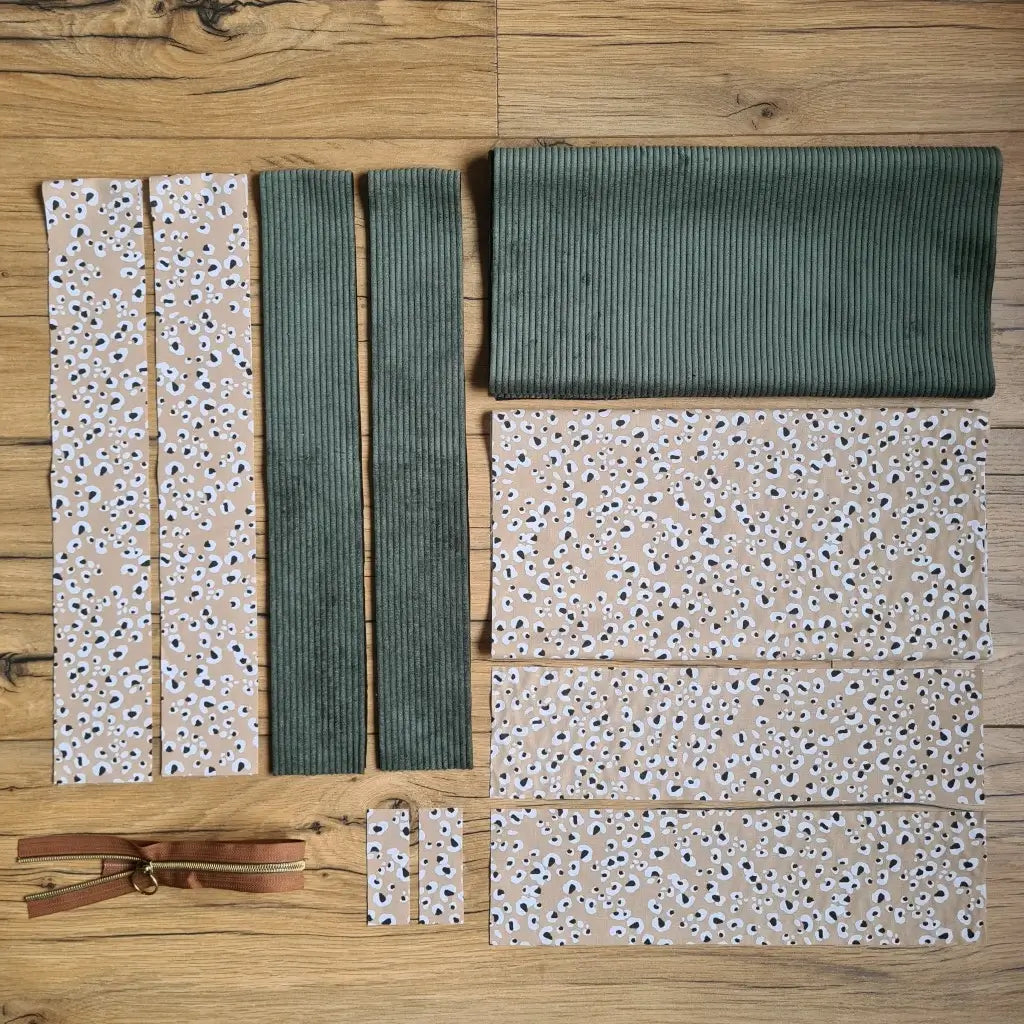 Kit "prêt à coudre" pour un tote-bag en velours côtelé au coloris vert avec une doublure en tissu à motif léopard. L'ensemble des pièces de tissu, déjà prédécoupées aux bonnes dimensions, sont disposées au sol et comprennent sept pièces en tissu à motif léopard et trois pièces en velours côtelé de couleur verte ainsi qu'une fermeture éclair marron.