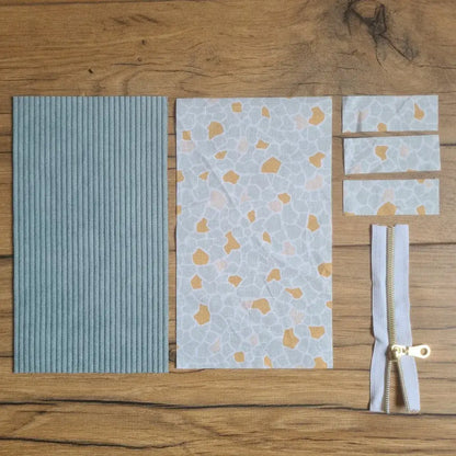 Kit "prêt à coudre" pour une trousse berlingot en velours côtelé au coloris bleu clair avec une doublure en tissu à motif argeo. L'ensemble des pièces de tissu, déjà prédécoupées aux bonnes dimensions, sont disposées au sol. A gauche, une pièce en velours côtelé bleu clair. A droite, quatre pièces en tissu imprimé à motif argeo ainsi qu'une fermeture éclair blanche.