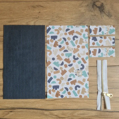 Kit "prêt à coudre" pour une trousse berlingot en velours côtelé au coloris bleu foncé avec une doublure en tissu à motif ptiwi. L'ensemble des pièces de tissu, déjà prédécoupées aux bonnes dimensions, sont disposées au sol. A gauche, une pièce en velours côtelé bleu foncé. A droite, quatre pièces en tissu imprimé à motif ptiwi ainsi qu'une fermeture éclair blanche.