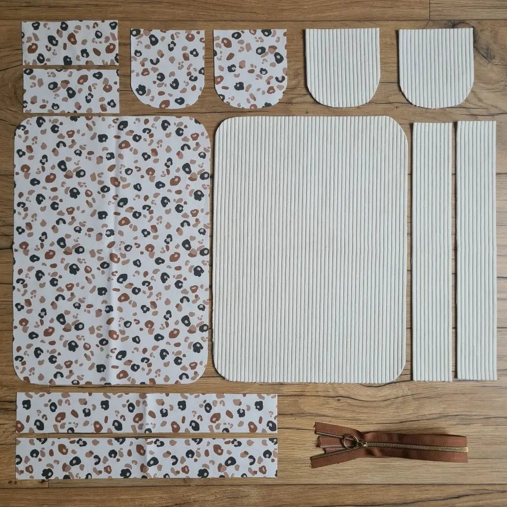 Kit "prêt à coudre" pour une trousse de toilette en velours côtelé au coloris beige avec une doublure en tissu à motif léopard. L'ensemble des pièces de tissu, déjà prédécoupées aux bonnes dimensions, sont disposées au sol. A gauche, sept pièces en tissu à motif léopard. A droite, cinq pièces en velours côtelé de couleur beige ainsi qu'une fermeture éclair marron.