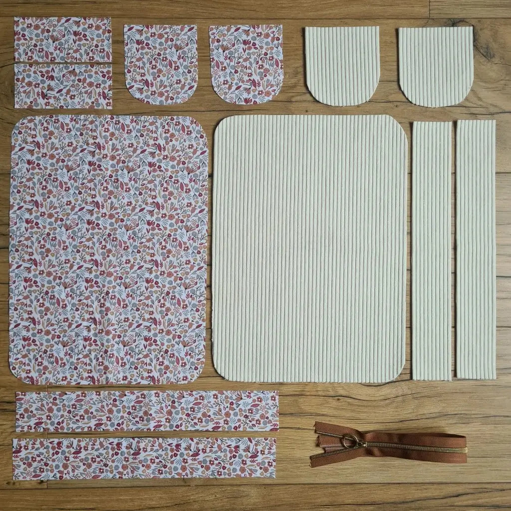 Kit "prêt à coudre" pour une trousse de toilette en velours côtelé au coloris beige avec une doublure en tissu à motif liberty. L'ensemble des pièces de tissu, déjà prédécoupées aux bonnes dimensions, sont disposées au sol. A gauche, sept pièces en tissu à motif liberty. A droite, cinq pièces en velours côtelé de couleur beige ainsi qu'une fermeture éclair marron.