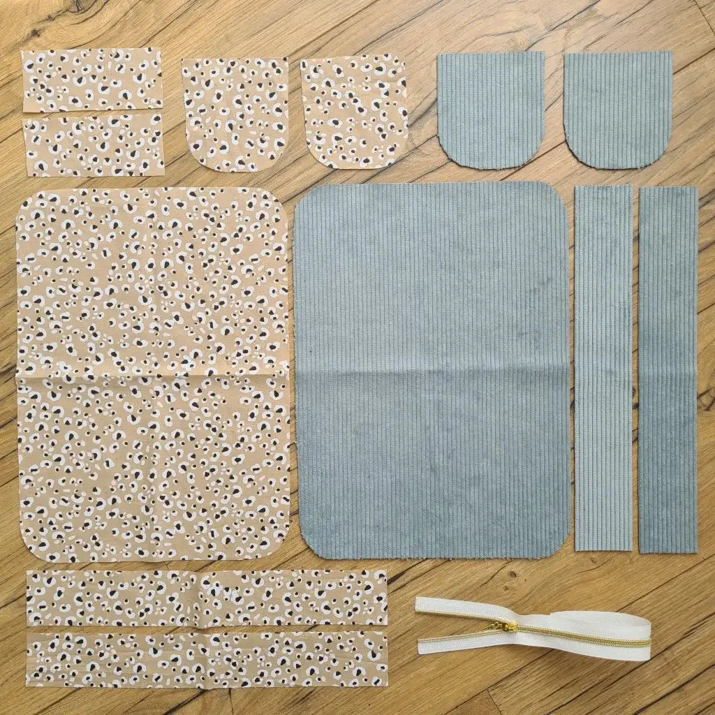 Kit "prêt à coudre" pour une trousse de toilette en velours côtelé au coloris bleu ciel avec une doublure en tissu à motif léopard. L'ensemble des pièces de tissu, déjà prédécoupées aux bonnes dimensions, sont disposées au sol. A gauche, sept pièces en tissu à motif léopard. A droite, cinq pièces en velours côtelé de couleur bleu ciel ainsi qu'une fermeture éclair blanche.