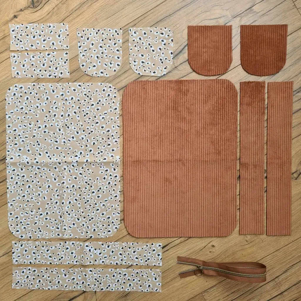 Kit "prêt à coudre" pour une trousse de toilette en velours côtelé au coloris marron avec une doublure en tissu à motif léopard. L'ensemble des pièces de tissu, déjà prédécoupées aux bonnes dimensions, sont disposées au sol. A gauche, sept pièces en tissu à motif léopard. A droite, cinq pièces en velours côtelé de couleur marron ainsi qu'une fermeture éclair marron.