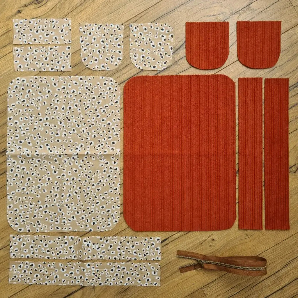 Kit "prêt à coudre" pour une trousse de toilette en velours côtelé au coloris terracotta avec une doublure en tissu à motif léopard. L'ensemble des pièces de tissu, déjà prédécoupées aux bonnes dimensions, sont disposées au sol. A gauche, sept pièces en tissu à motif léopard. A droite, cinq pièces en velours côtelé de couleur terracotta ainsi qu'une fermeture éclair marron.