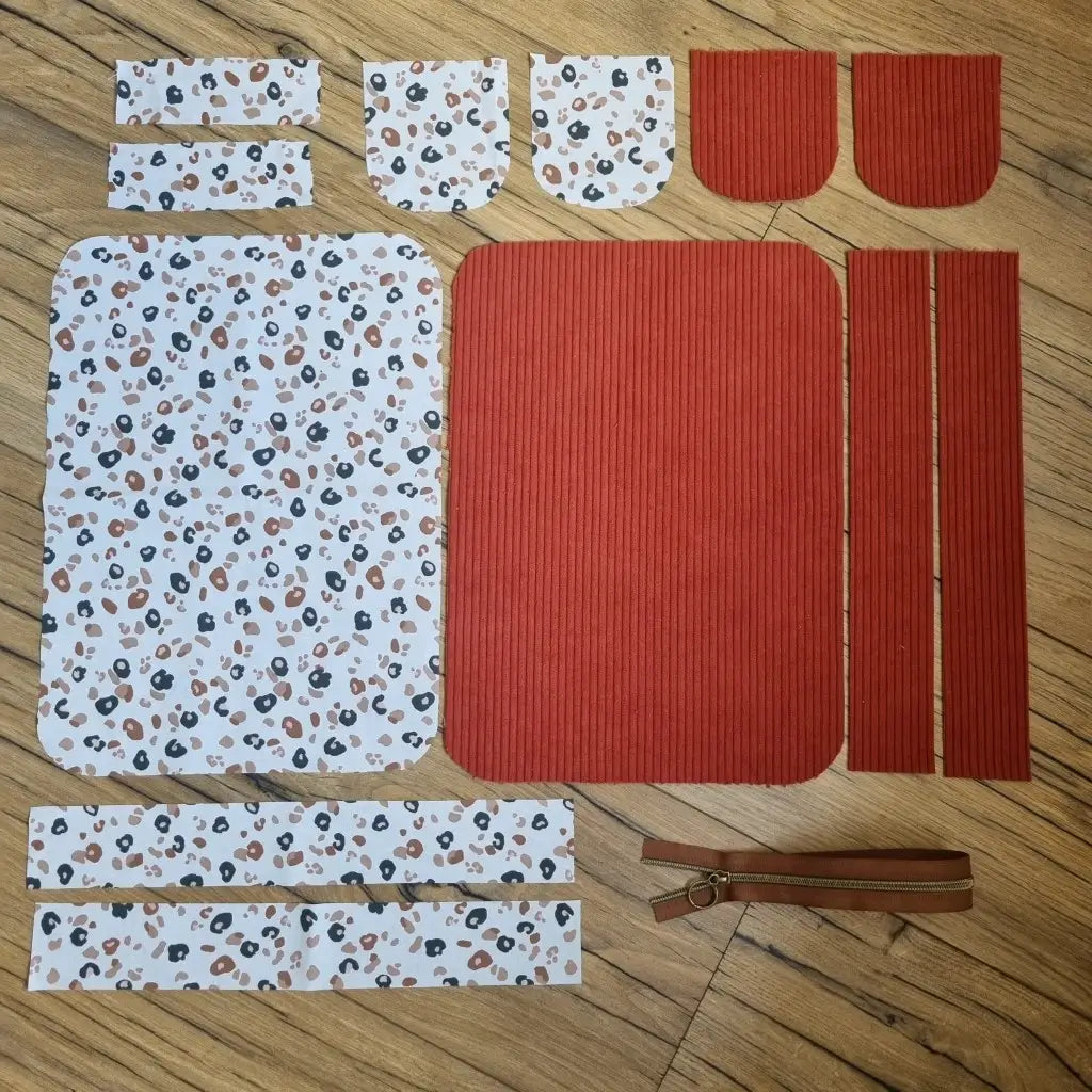 Kit "prêt à coudre" pour une trousse de toilette en velours côtelé au coloris terracotta avec une doublure en tissu à motif léopard. L'ensemble des pièces de tissu, déjà prédécoupées aux bonnes dimensions, sont disposées au sol. A gauche, sept pièces en tissu à motif léopard. A droite, cinq pièces en velours côtelé de couleur terracotta ainsi qu'une fermeture éclair marron.