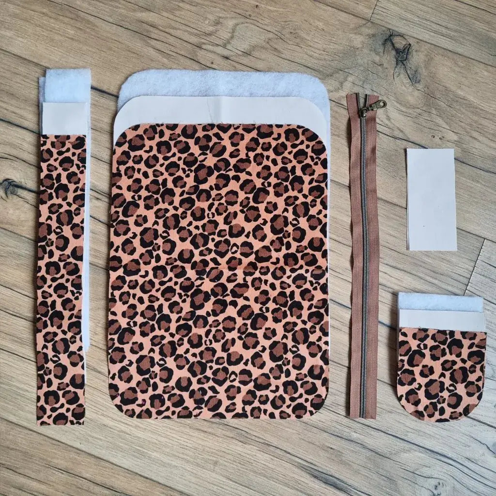 Kit couture trousse léopard : coupons de tissu motif animal, doublure beige, ouatine et zip brun sur bois.