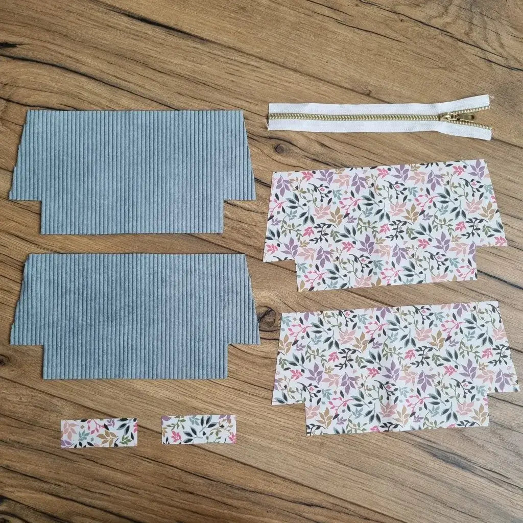 Kit de couture DIY pour trousse d’école zippée composé de deux pièces en velours côtelé bleu clair, quatre coupons de coton enduit fleuri pastel, deux petites bandes assorties et une fermeture éclair blanche avec zip doré. Les éléments sont soigneusement étalés sur un sol en bois, prêts à être assemblés pour créer une trousse d'école personnalisée avec doublure, idéale pour offrir ou préparer la rentrée scolaire.