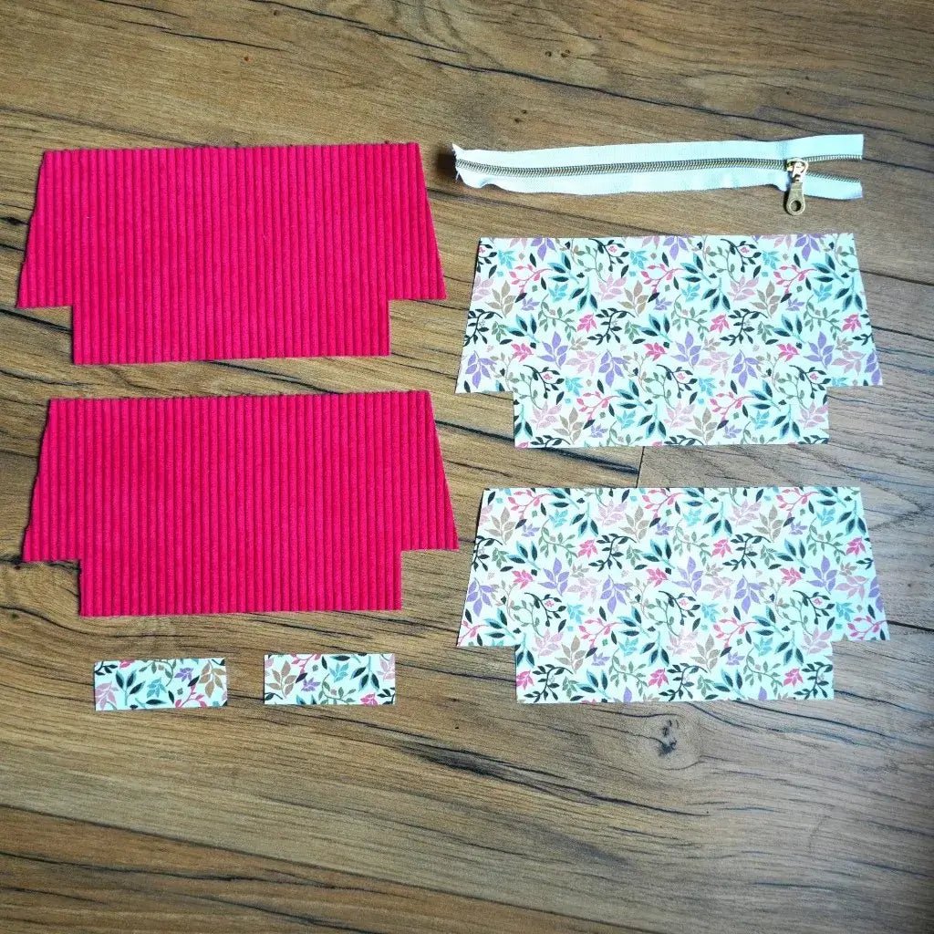 Kit de couture pour trousse scolaire comprenant des pièces de velours côtelé framboise et de coton imprimé fleuri, ainsi qu’une fermeture éclair blanche avec curseur doré, disposés à plat sur un sol en bois. Ce lot prêt à assembler est idéal pour réaliser une trousse originale et personnalisée, parfaite pour la rentrée ou comme accessoire créatif fait main.